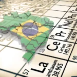 Mapa das Terras Raras no Brasil, com o mapa do nosso país e a bandeira em cima de uma Tabela Periódica. A imagem foca nos elementos químicos que são as terras raras, mostrando que o Brasil tem essa riqueza