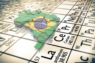 Mapa das Terras Raras no Brasil, com o mapa do nosso país e a bandeira em cima de uma Tabela Periódica. A imagem foca nos elementos químicos que são as terras raras, mostrando que o Brasil tem essa riqueza