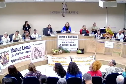 Audiência pública em Minas Gerais sobre a Ferrovia da Cedro, com moradores de Mateus Leme e região presentes, segurando cartazes de protesto contra o projeto.