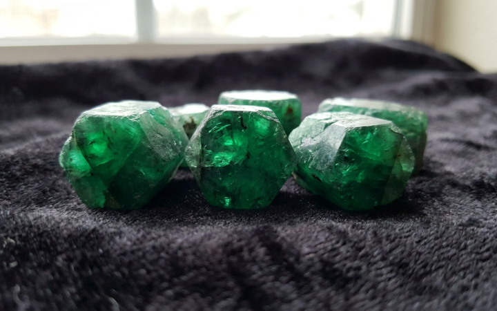 Cristais de esmeralda brasileira bruta verde intenso sobre veludo escuro com iluminação natural destacando as facetas